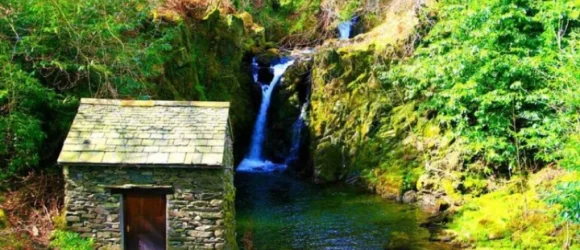 Small stone building by a forest waterfall.