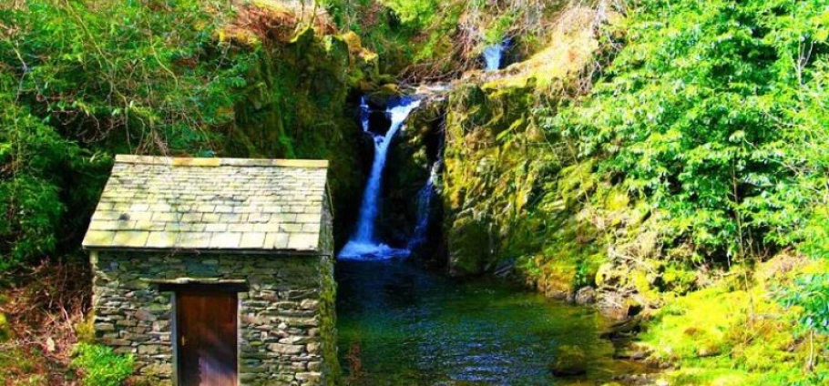 Small stone building by a forest waterfall.