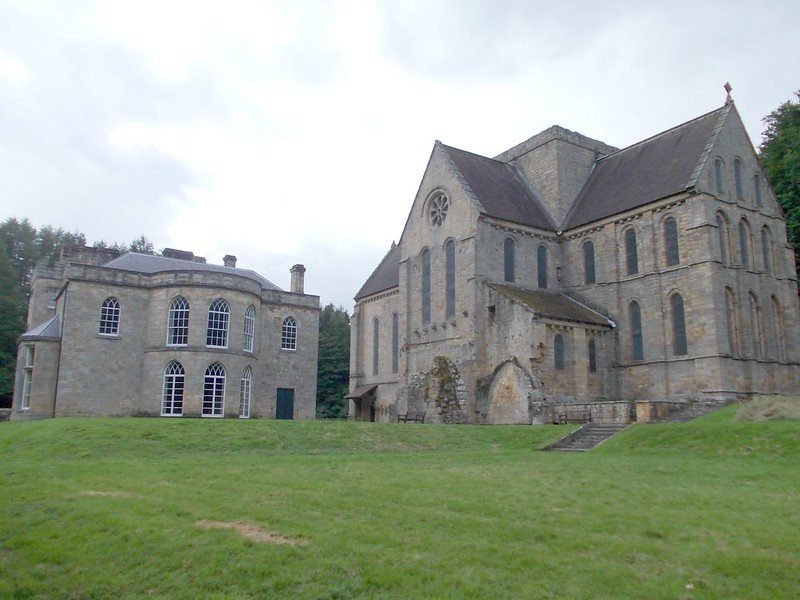 Historic stone building with a large church featuring arched windows and a circular rose window, set in a grassy area.