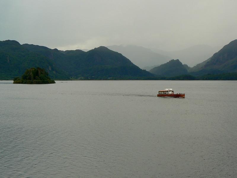 Derwentwater, A boat on a lake with mountainous islands in the background on a cloudy day.