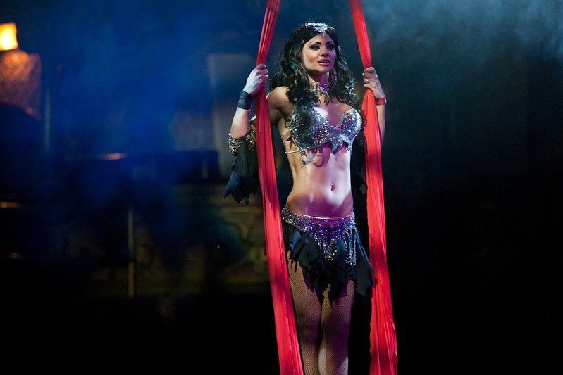 Aerial performer in a sparkling costume holding red silk ropes on stage.