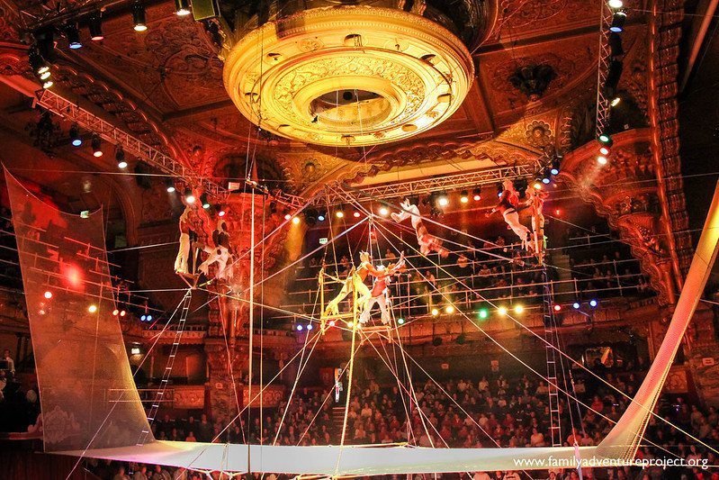 Acrobats performing on a high wire in an ornate, illuminated theatre setting.