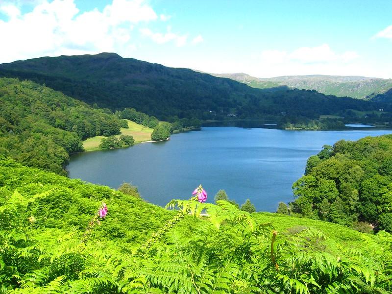 A scenic view of a lake surrounded by green hills and dense foliage under a partly cloudy sky.