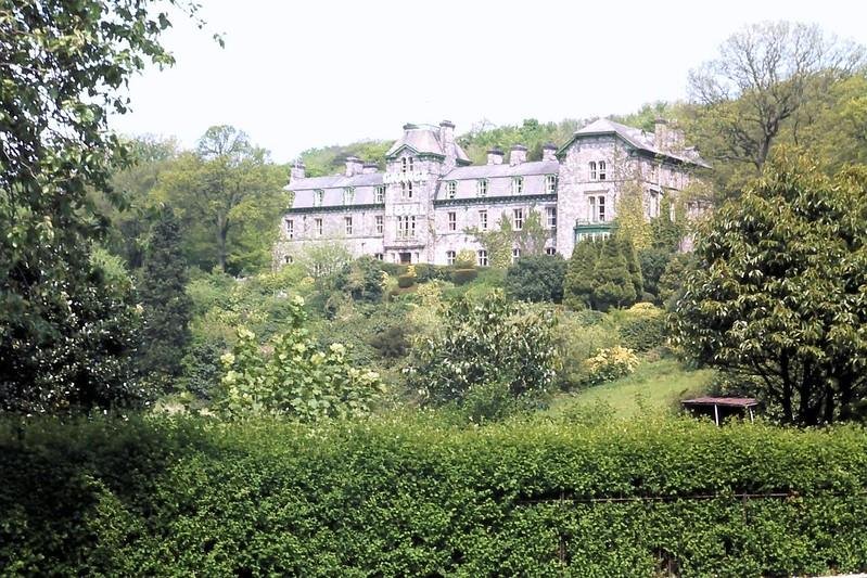 Large historic stone mansion surrounded by lush greenery and trees.