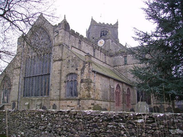 Cartmel Priory | Medieval stone church building with a tall tower and large arched windows, surrounded by a stone wall.