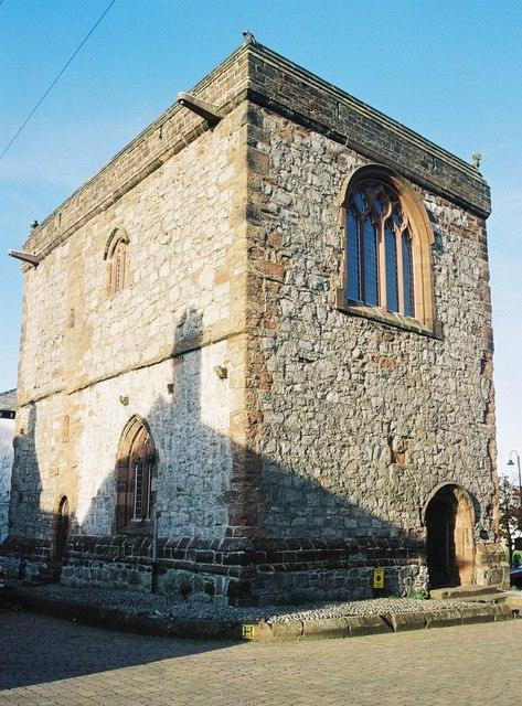 Old stone building with Gothic windows and arched entrance, against a clear blue sky.