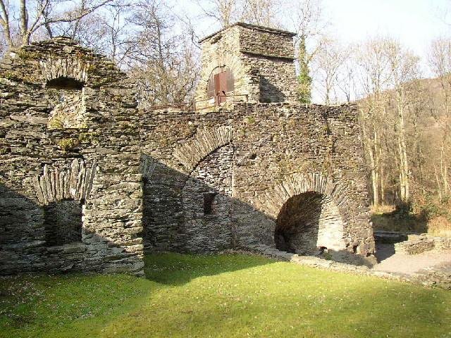 Ruins of a historic stone-built blast furnace surrounded by trees.