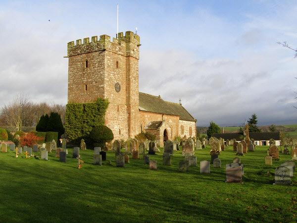 Great Salkeld | Stone church with a crenellated tower surrounded by a graveyard with headstones on a grassy field under a partly cloudy sky.