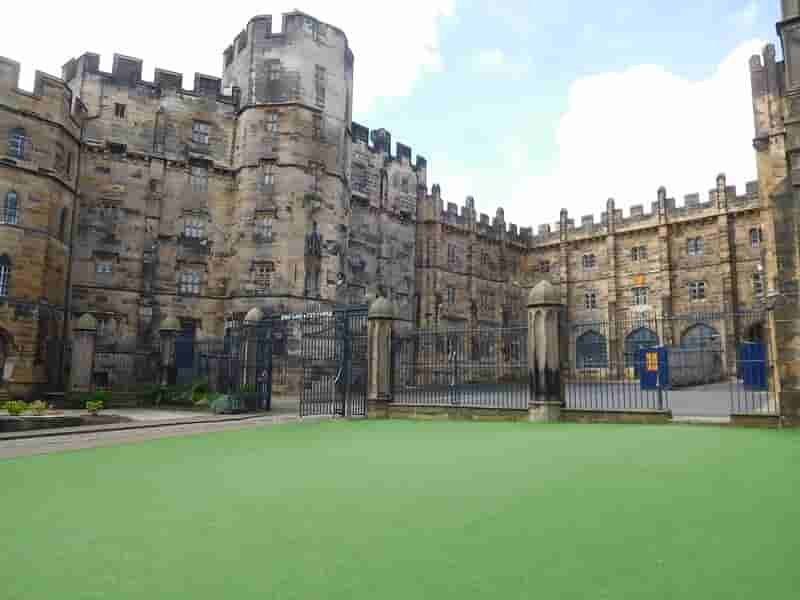 Exterior view of a historic stone castle with crenellated towers, metal gates, and a neatly trimmed lawn in the foreground.