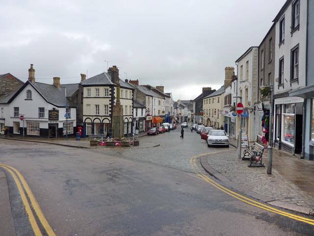 Market Street, Ulverston | A cobblestone street with buildings and shops lined on both sides in a small town on a cloudy day.