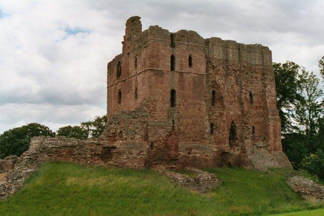 Ruins of a stone castle with partially collapsed walls, surrounded by grass and trees.