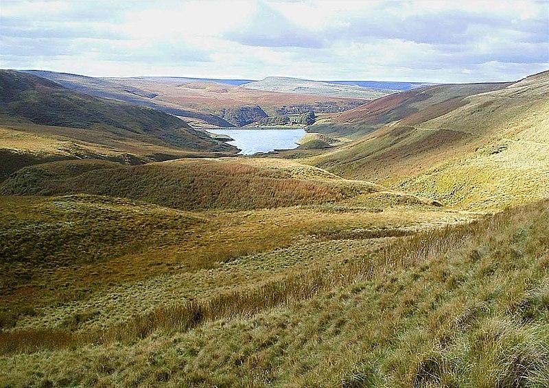 Haltwhistle | Rolling hills covered in grass and heath lead down to a lake surrounded by more hills in the background, under a cloudy sky.