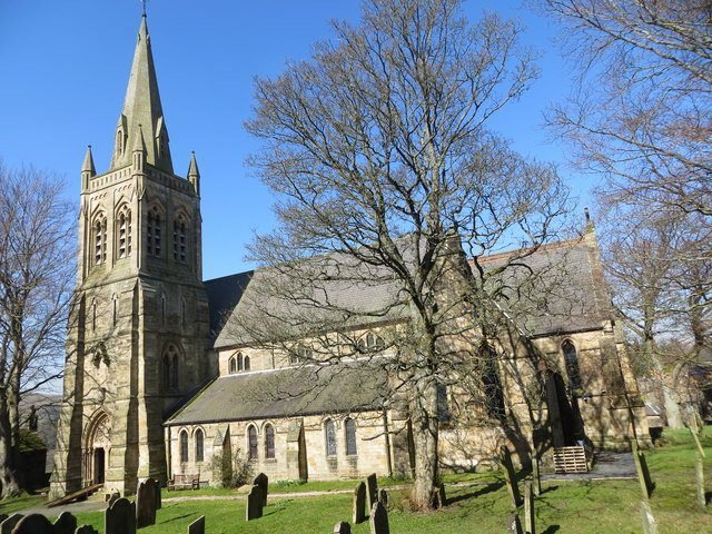 Stone church with a tall steeple and several pointed towers surrounded by bare trees and gravestones on a sunny day
