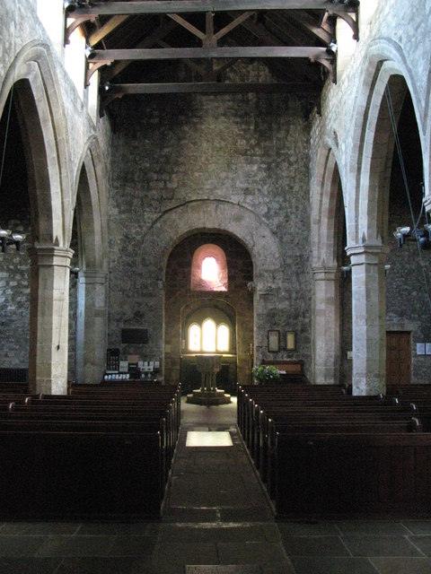 Interior of an old stone church with wooden pews, arched doorways, and stained glass windows.