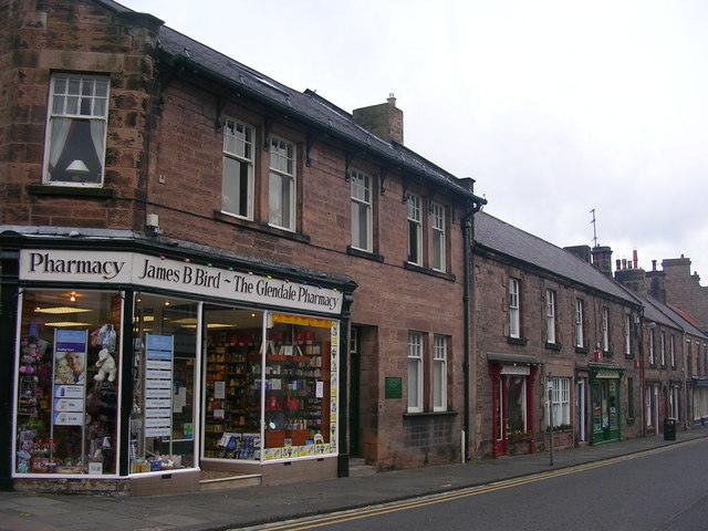 Wooler a Street view of a stone building with a pharmacy named "James B Bird - The Glendale Pharmacy" in the foreground and additional shops along the street.