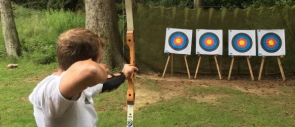 Person aiming a bow and arrow at a row of archery targets outdoors.