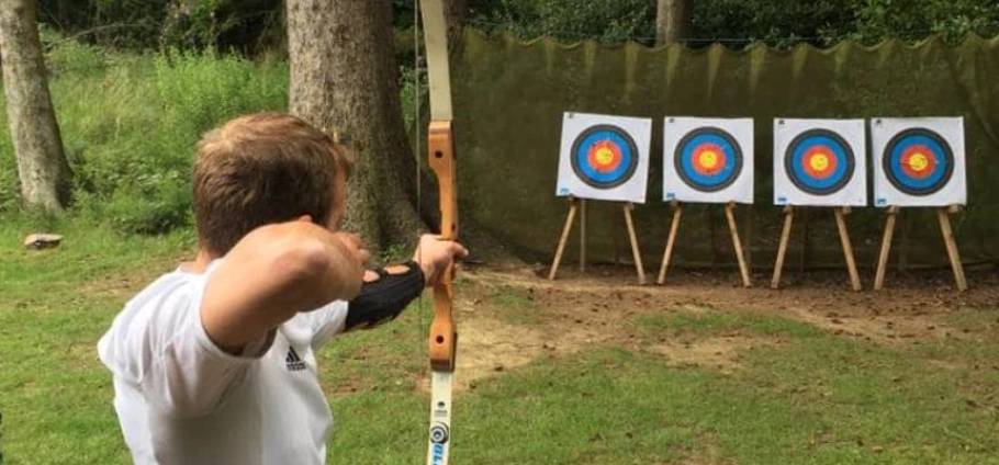 Person aiming a bow and arrow at a row of archery targets outdoors.