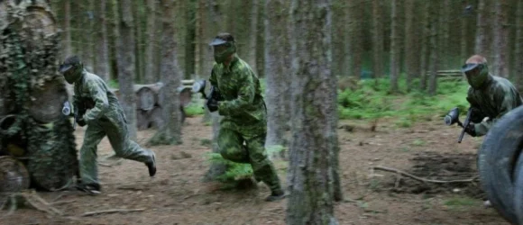 Three people in camouflage gear playing paintball in a forest.