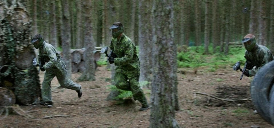 Three people in camouflage gear playing paintball in a forest.