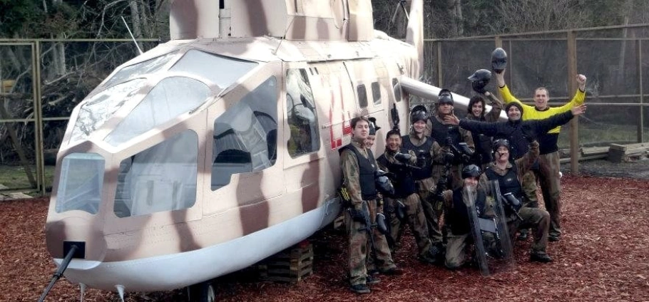 A group of people in paintball gear standing in front of a helicopter model.