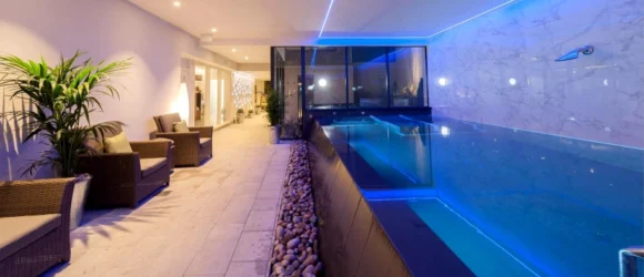 Indoor pool area with modern seating, ambient blue lighting, and decorative plants.