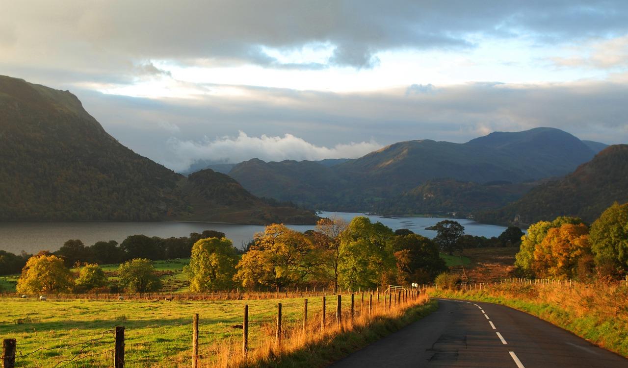 Kendal Road leading to a lake with mountains in the background and trees with autumn foliage on both sides.