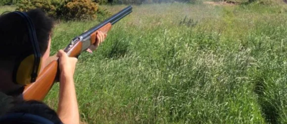 Person wearing hearing protection shooting a double-barrel shotgun in a grassy field.