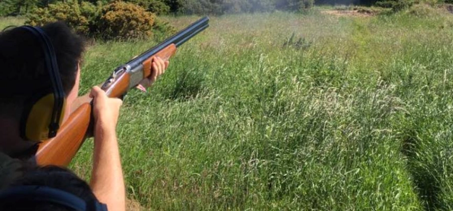 Person wearing hearing protection shooting a double-barrel shotgun in a grassy field.