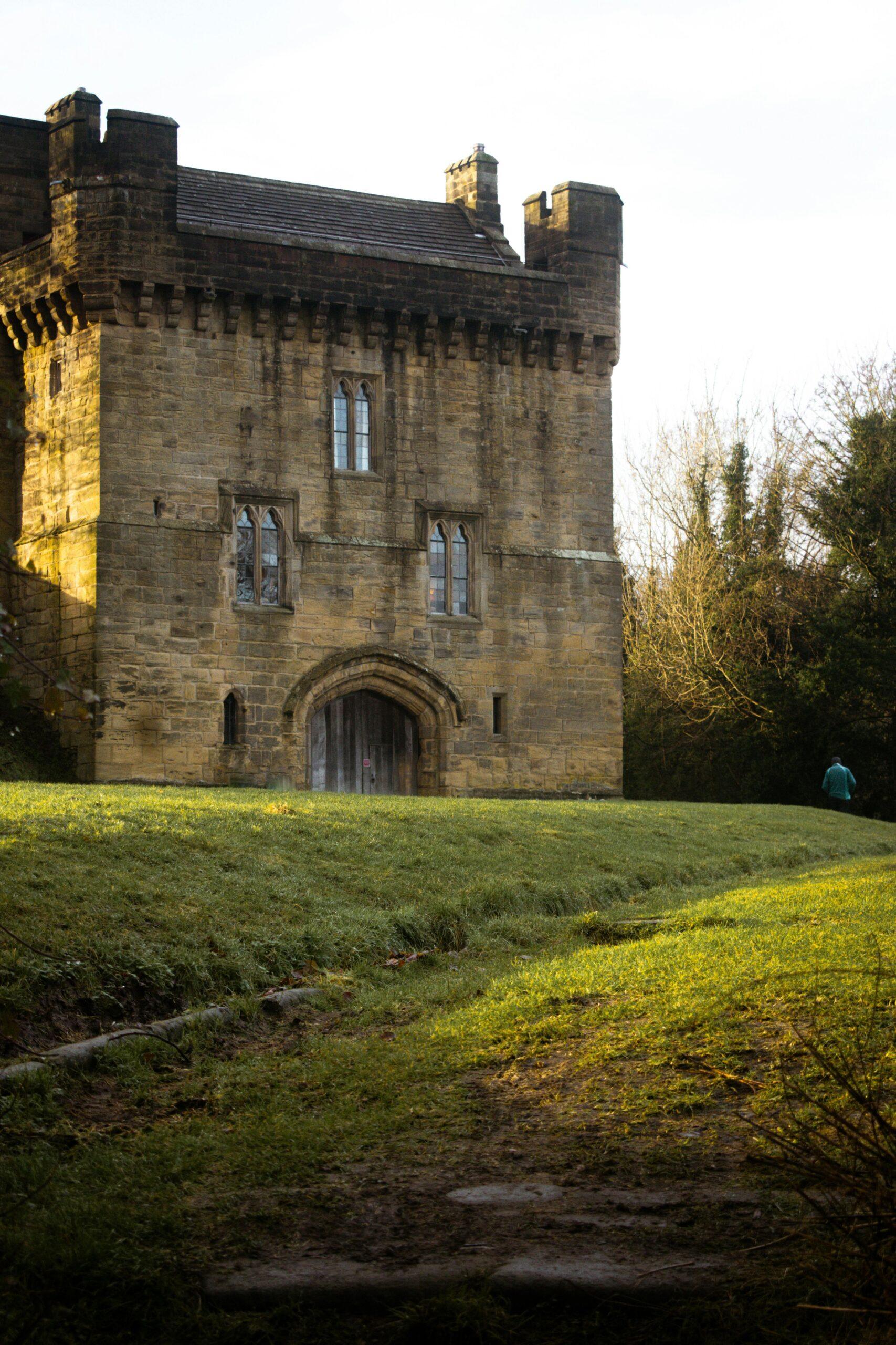 a stone building with a person walking in the grass