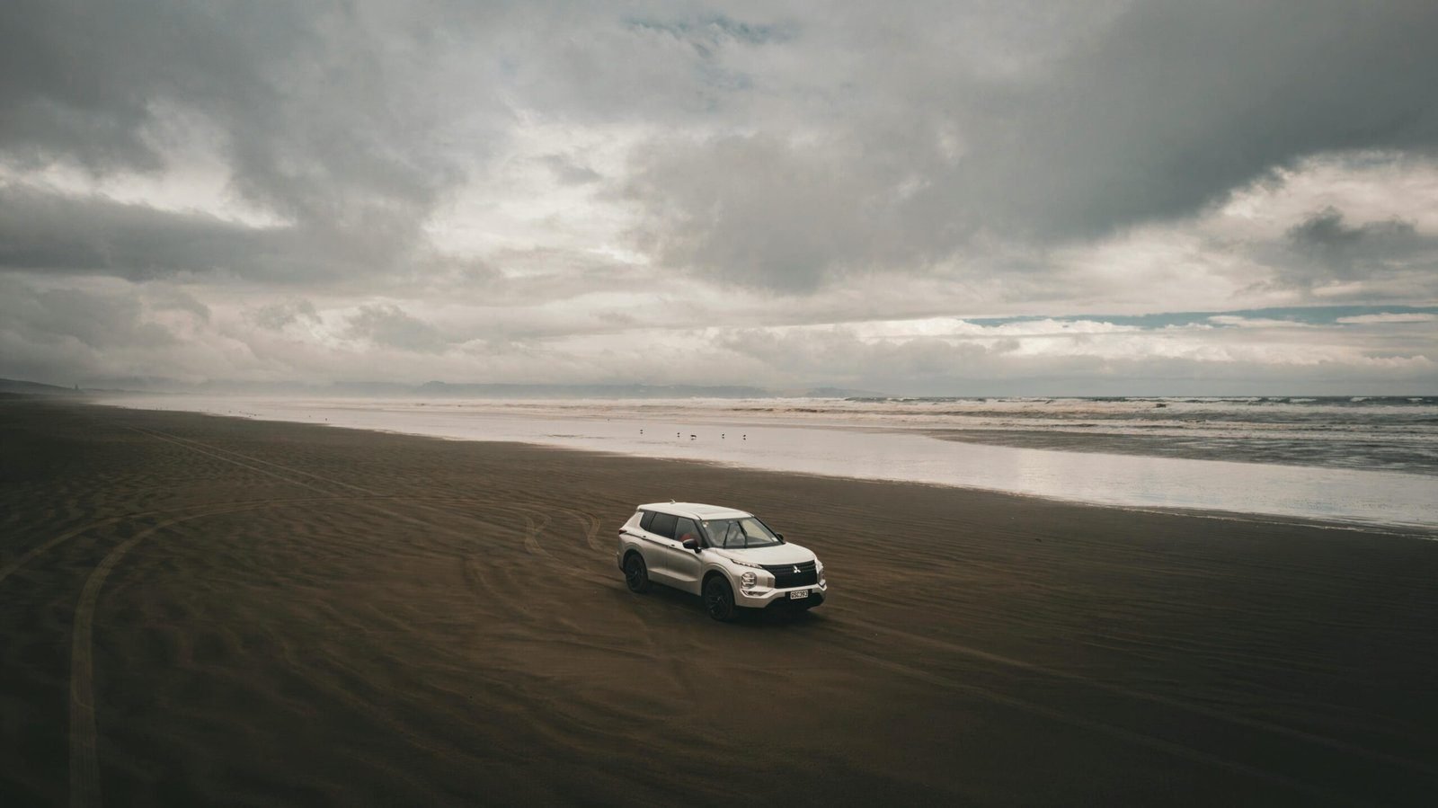 UK Car Rental Deals 1 UK Car Rental Deals: White SUV parked on a dark sandy beach under a cloudy sky with waves in the background