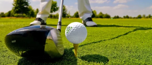 Golf club, ball, and tee on a golf course with a golfer's legs in the background.