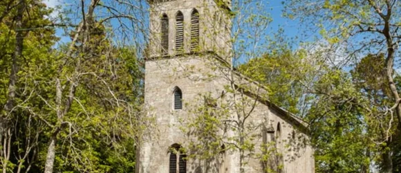 Stone church with a tower surrounded by trees and a stone wall.