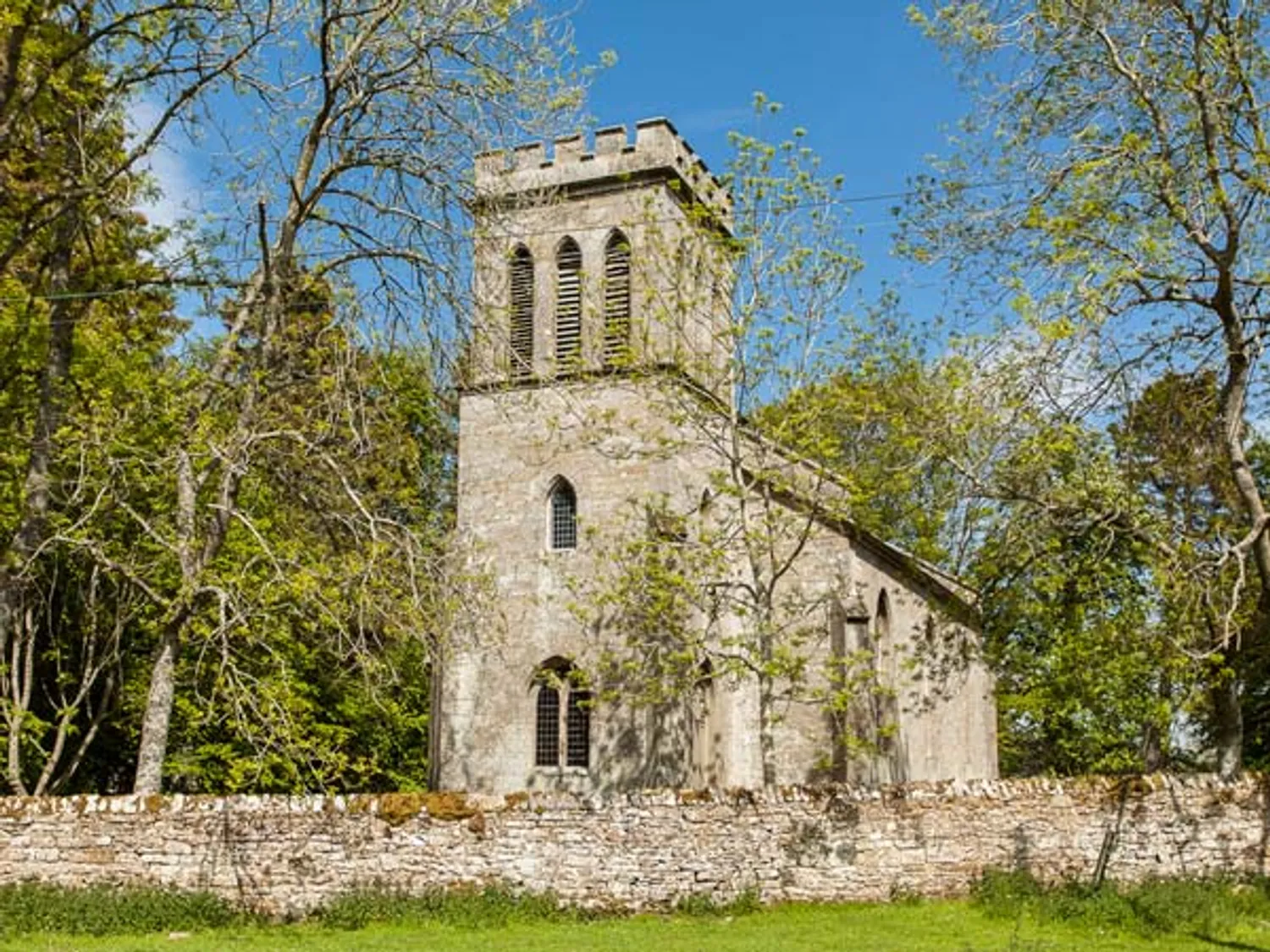 Stone church with a tower surrounded by trees and a stone wall.