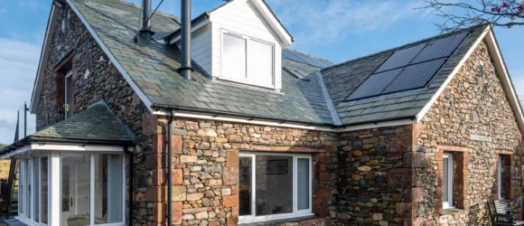 Stone cottage with a slate roof, solar panels, and a small garden with a bench.