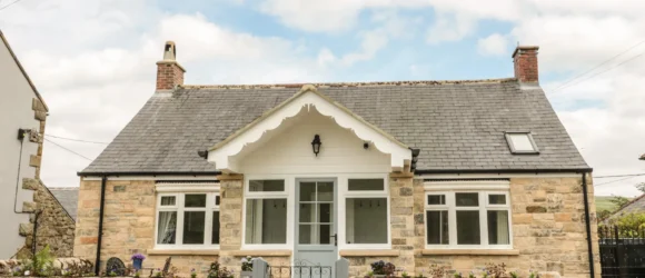 Stone cottage with a slate roof, front porch, and small garden enclosed by a low stone wall and gate.