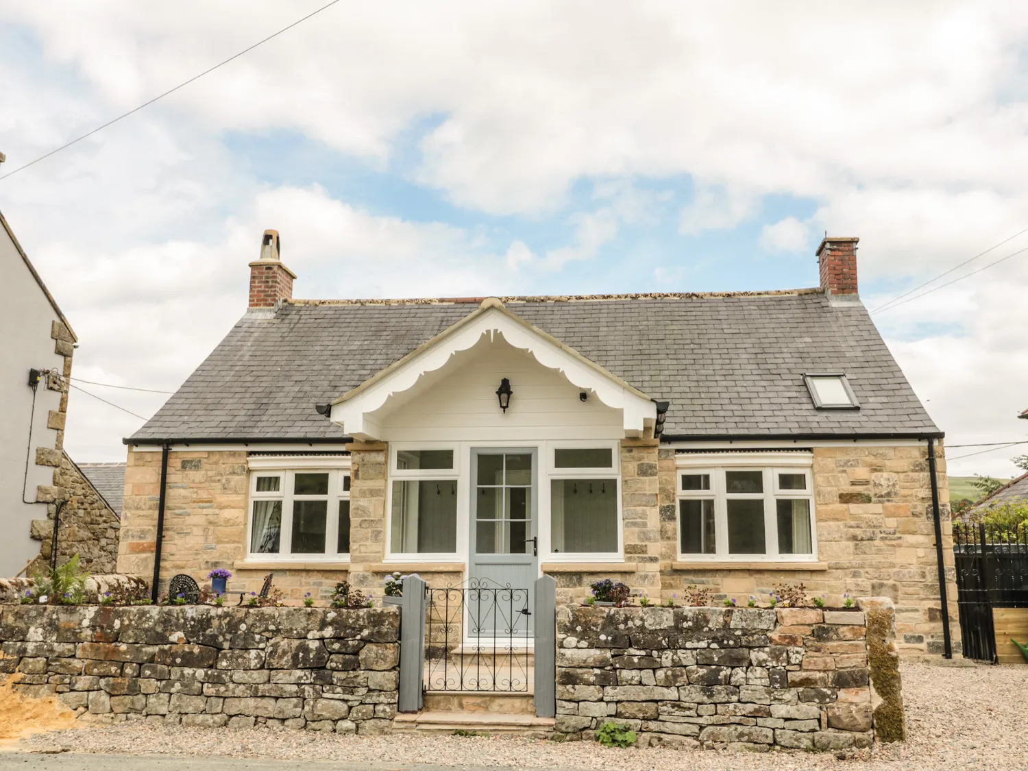 Stone cottage with a slate roof, front porch, and small garden enclosed by a low stone wall and gate.