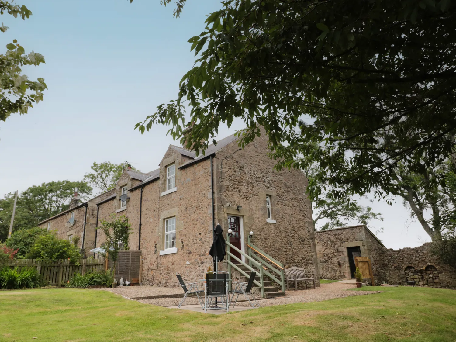 Stone house with gabled roofs, surrounded by greenery, with outdoor seating and a small garden area.