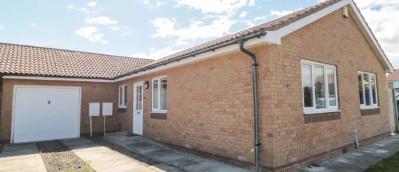 Single-storey house with brick exterior, tiled roof, attached garage, and paved driveway.