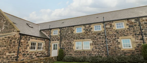 Stone cottage with a slate roof and multiple windows on a grassy lawn.