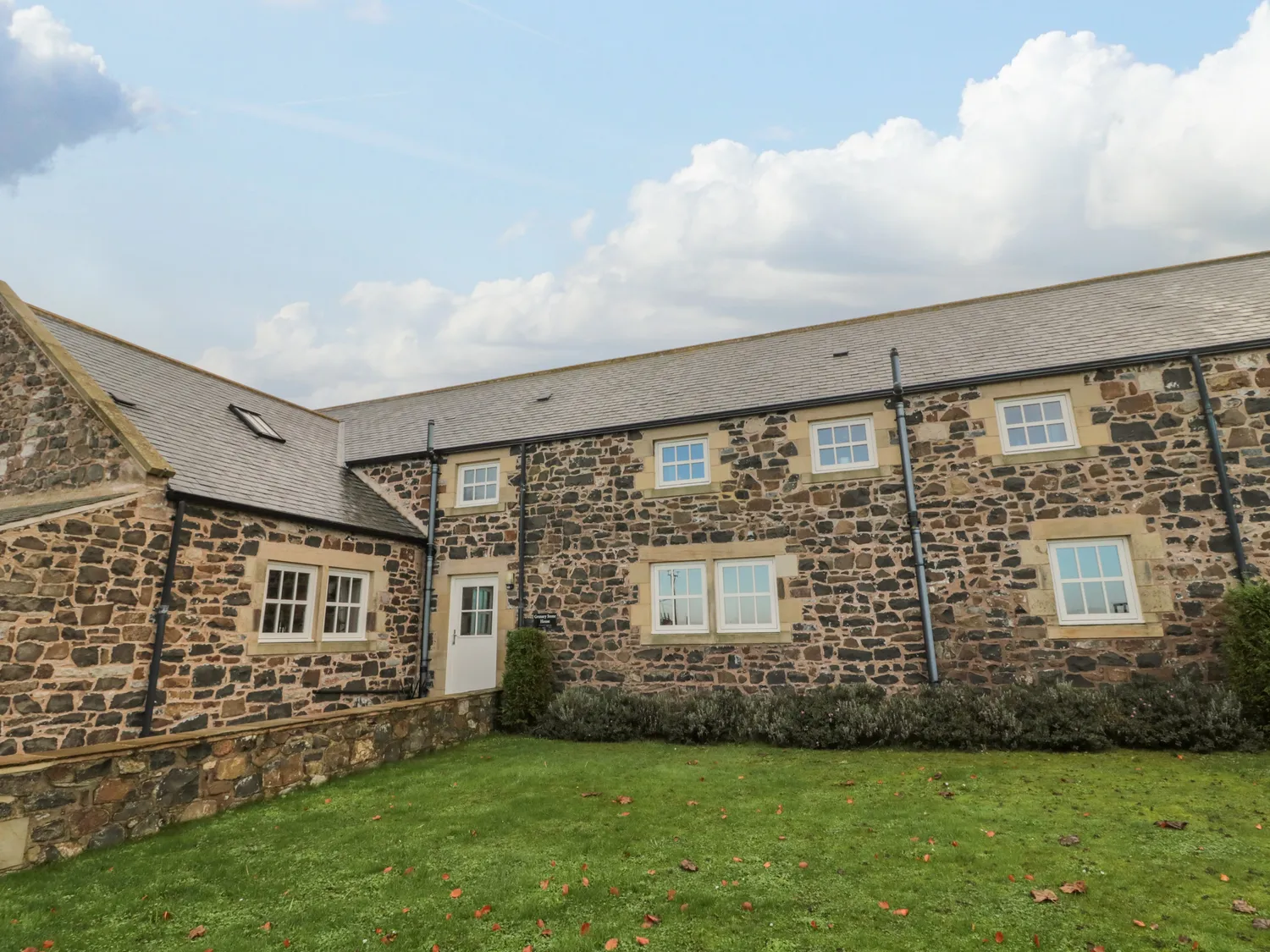 Stone cottage with a slate roof and multiple windows on a grassy lawn.