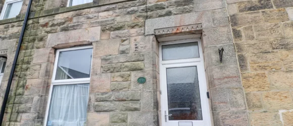 Stone facade of a terraced house with white-framed windows and a white door.