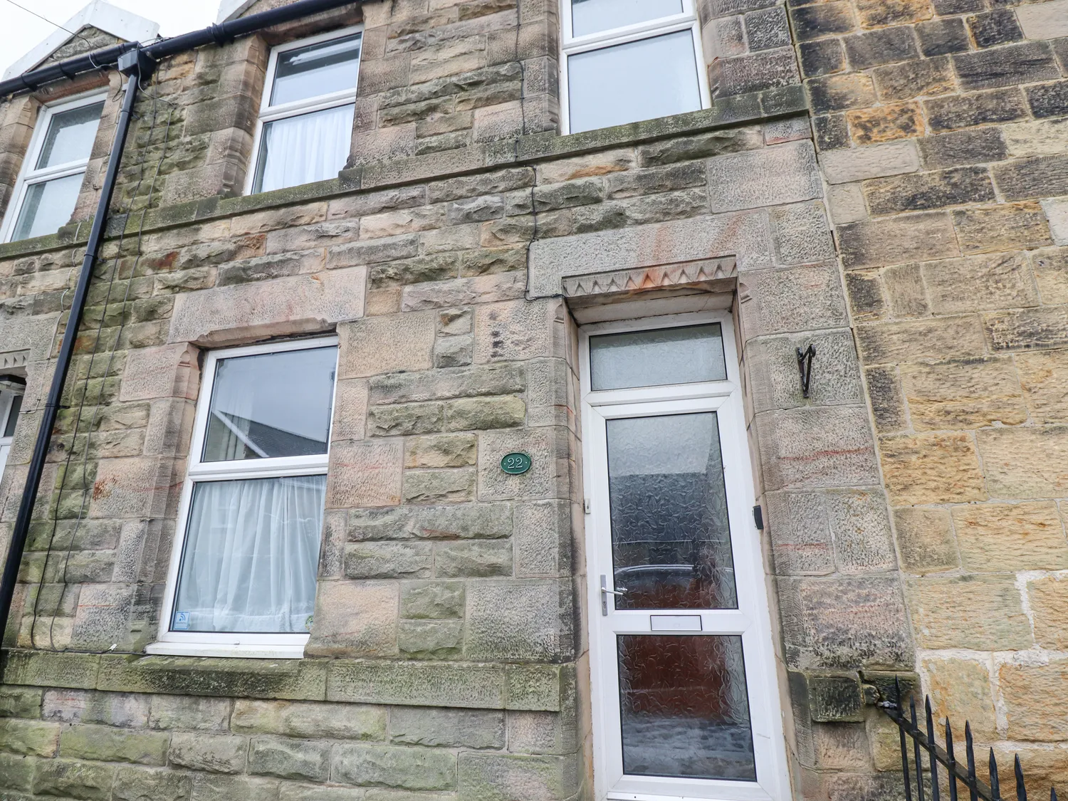 Stone facade of a terraced house with white-framed windows and a white door.