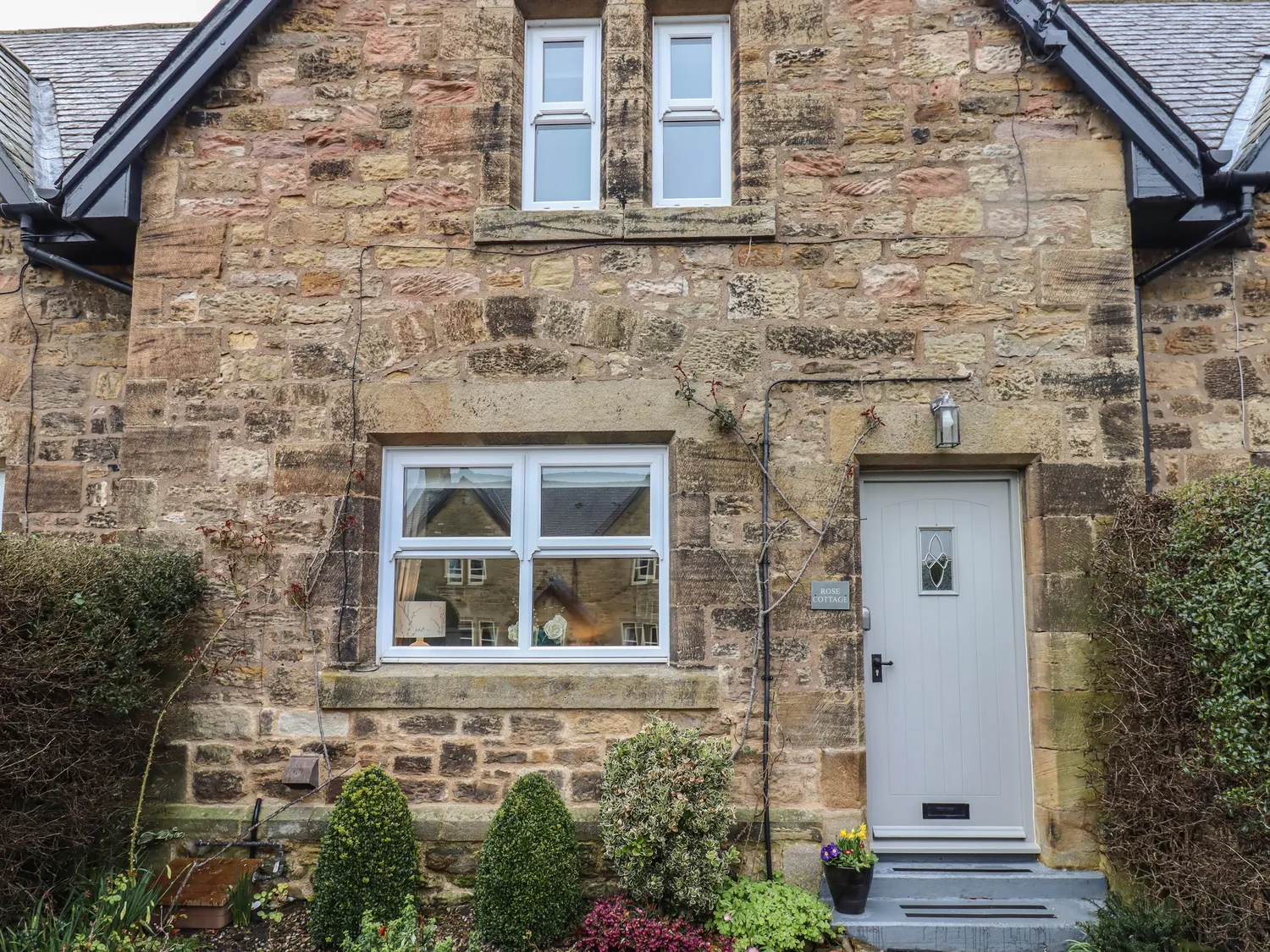 Stone cottage facade with a grey door, a window to the left of the door, and a smaller window above.