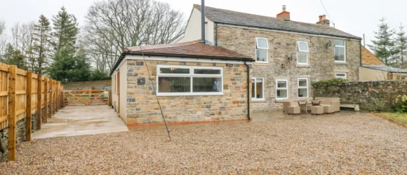 Stone house with an extension, gravel driveway, and outdoor seating area.