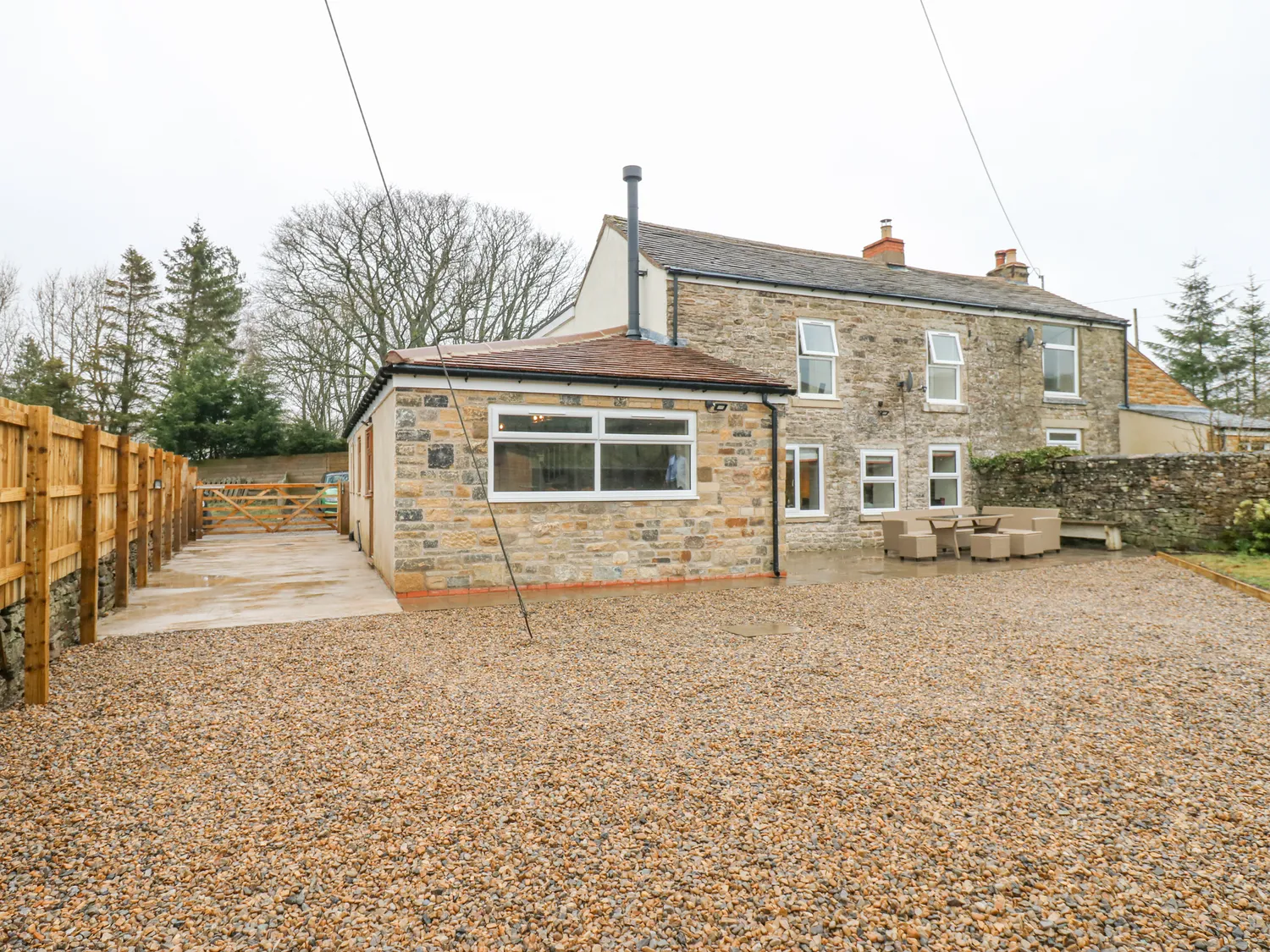 Stone house with an extension, gravel driveway, and outdoor seating area.