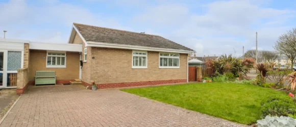 Single-storey brick house with a pitched roof, large paved driveway, and well-kept front lawn.