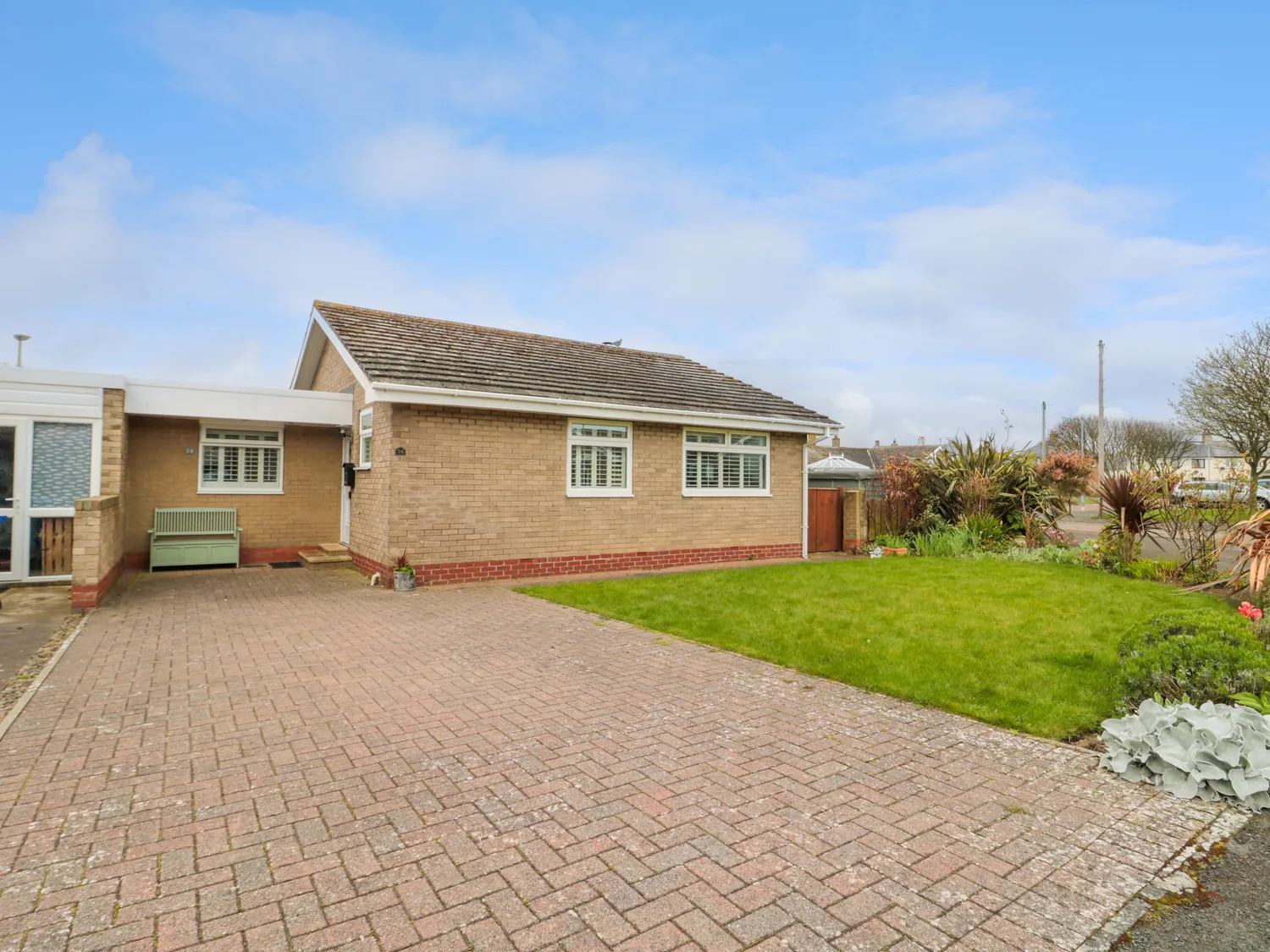 Single-storey brick house with a pitched roof, large paved driveway, and well-kept front lawn.