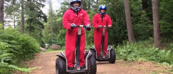 Two people in red jumpsuits riding Segways in a wooded area.