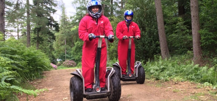 Two people in red jumpsuits riding Segways in a wooded area.