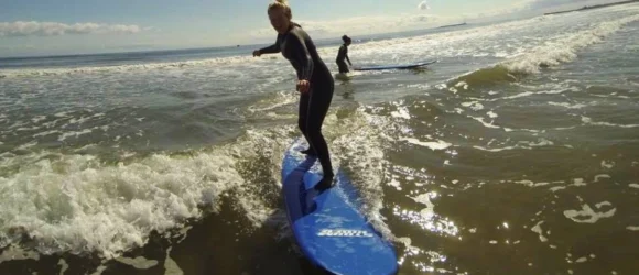 Person surfing on a blue surfboard in the ocean, with another surfer in the background.